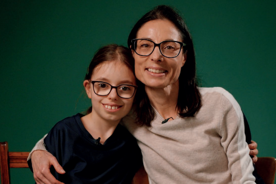 A mother and daughter smile with their arms around each other