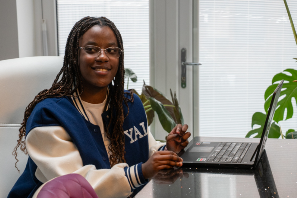 A young woman smiles, sitting infront of a laptop