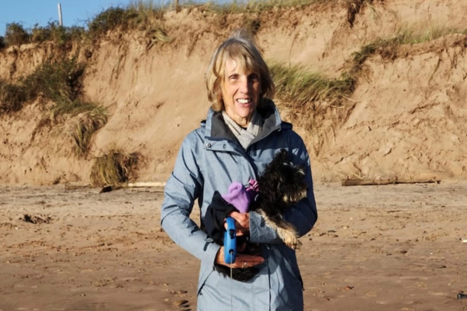 Smiling woman on a beach holding her dog