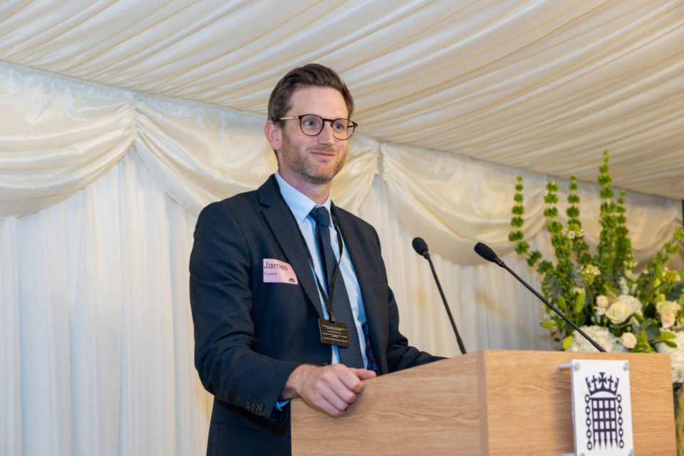 James stands at a lecturn smiling