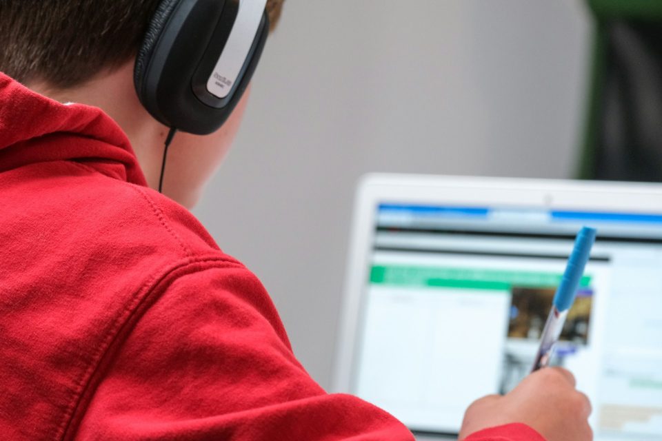 A person earing headphones makes notes from a computer