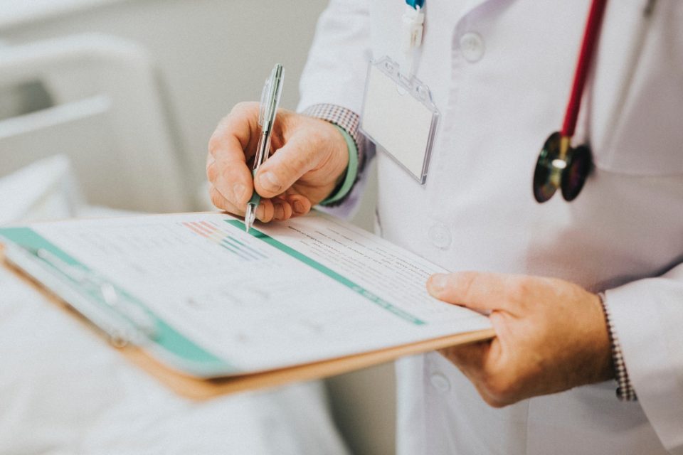 A health professional holds a clipboard while wearing a stethoscope