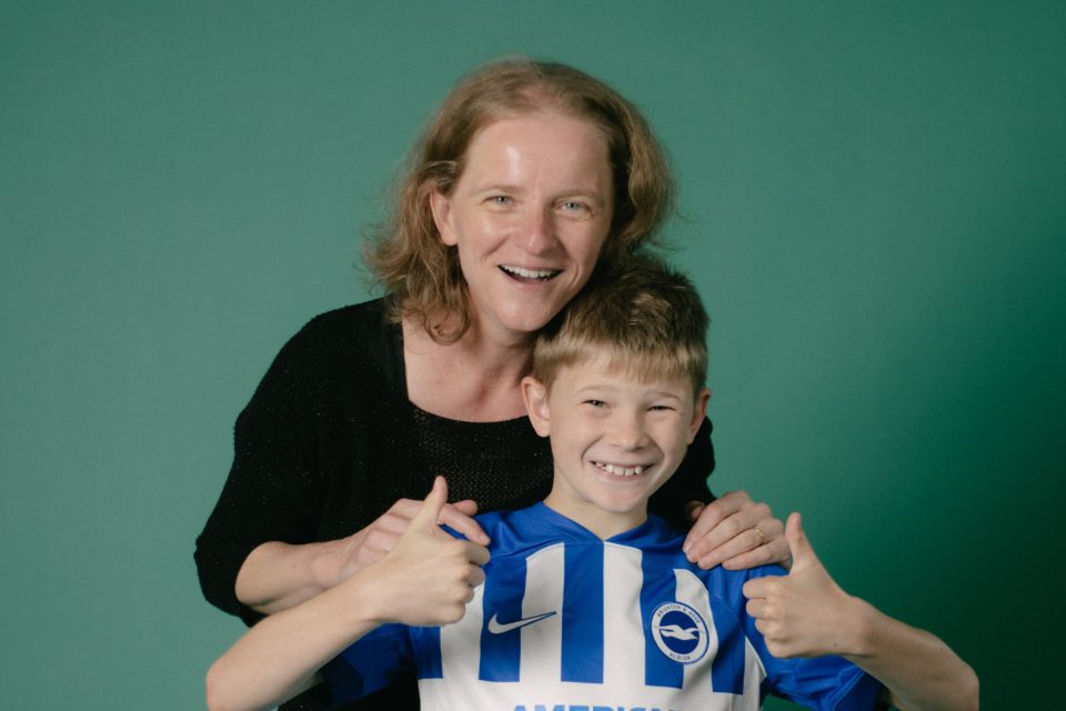 Top autism research priorities: a smiling mother hugs her son from behind as he gives a thumbs up to the camera