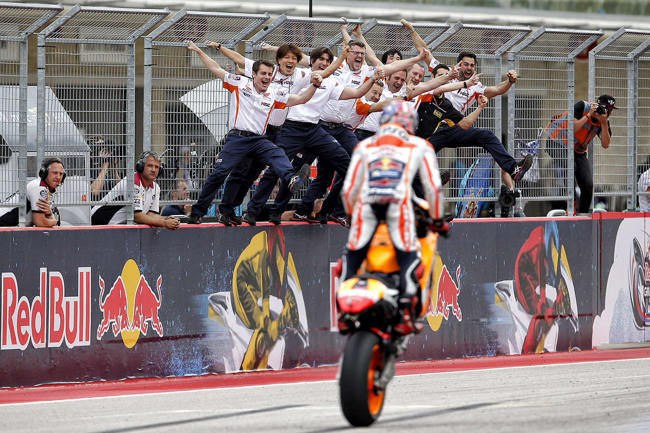 Marc Márquez hace un caballito en meta para celebrar el éxito con su equipo.