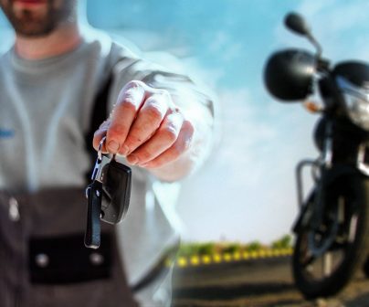 hombre con el brazo extendido ofrece a cámara las llaves de una moto naked que vemos aparcada en segundo plano