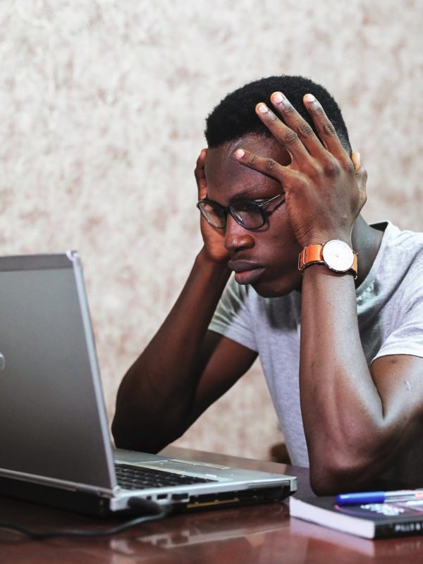 A person in front of a laptop with a worried expression and their hands gripping the sides of their head