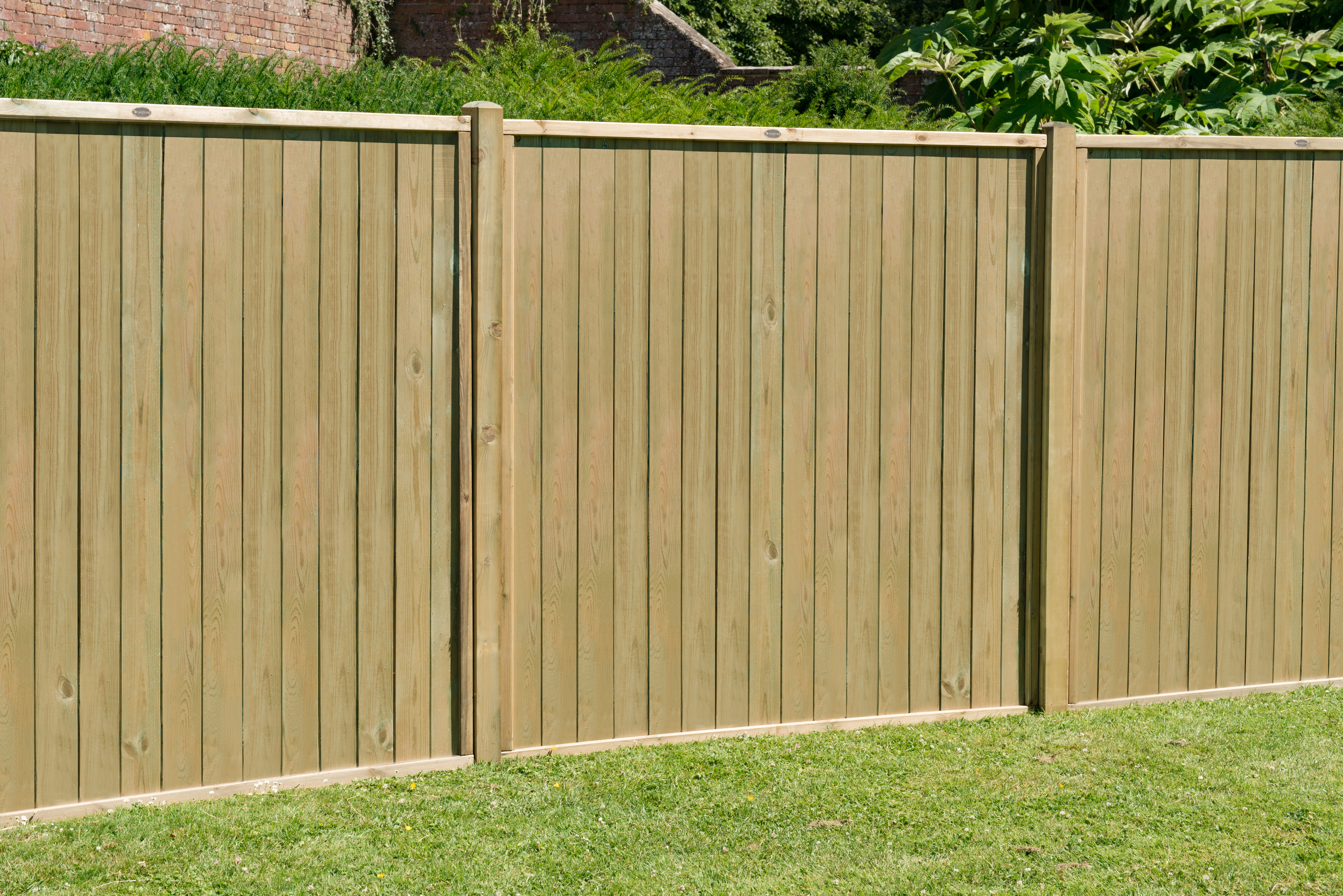 an image of a wooden timber fence with circular, concrete posts amongst green grass.