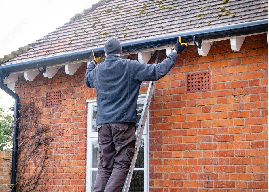 A man using tools to measure some gutters outside his house to be able to replace them.
