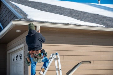 A man replacing some gutters outside someones house, using a step-ladder to get up.
