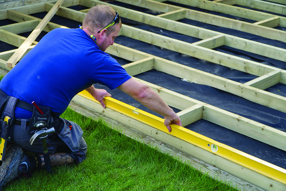 A laying a decking sub frame over the soil in the garden and surrounded by joists
