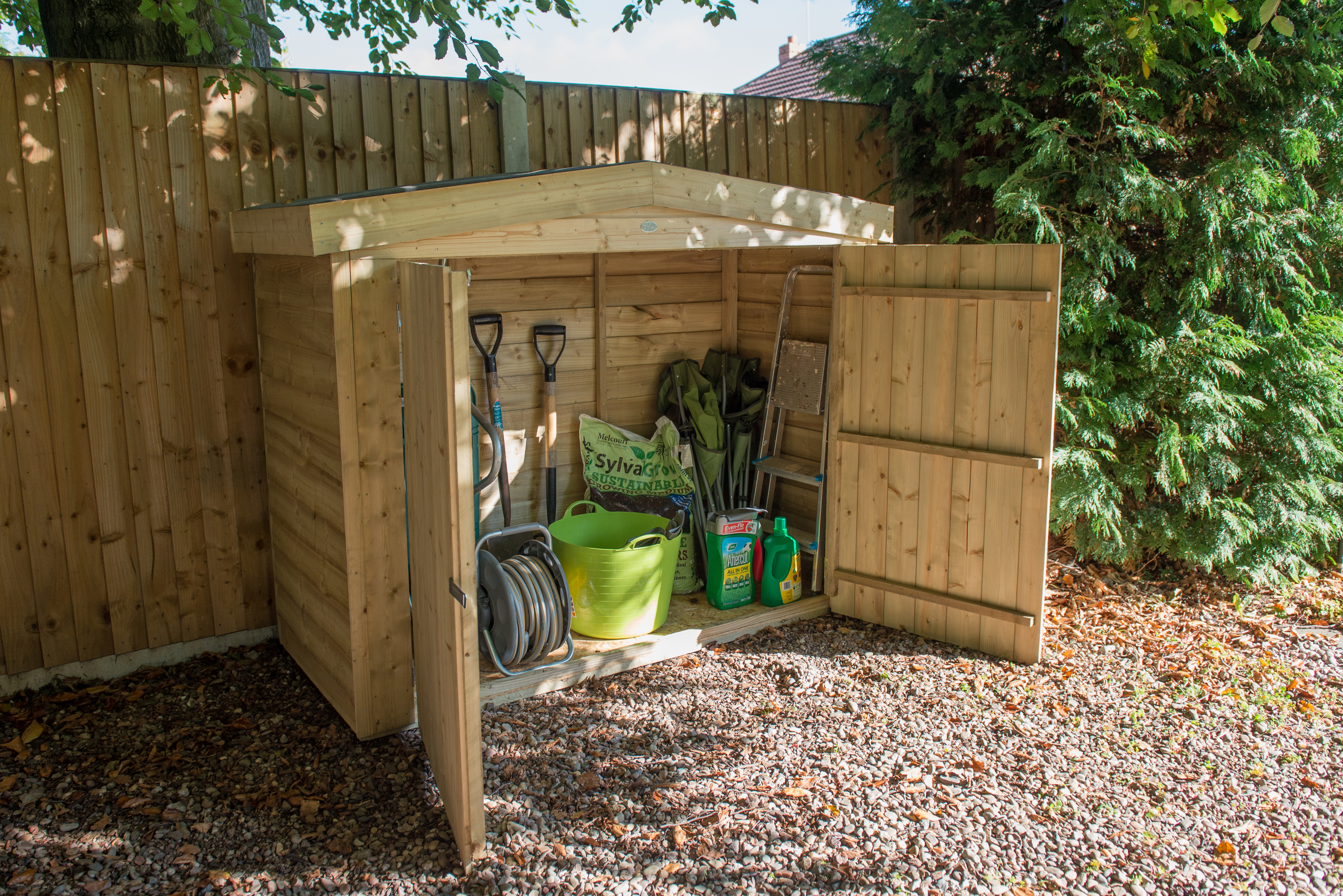 A wooden garden storage box with a roof, holding a bright green bike within it.