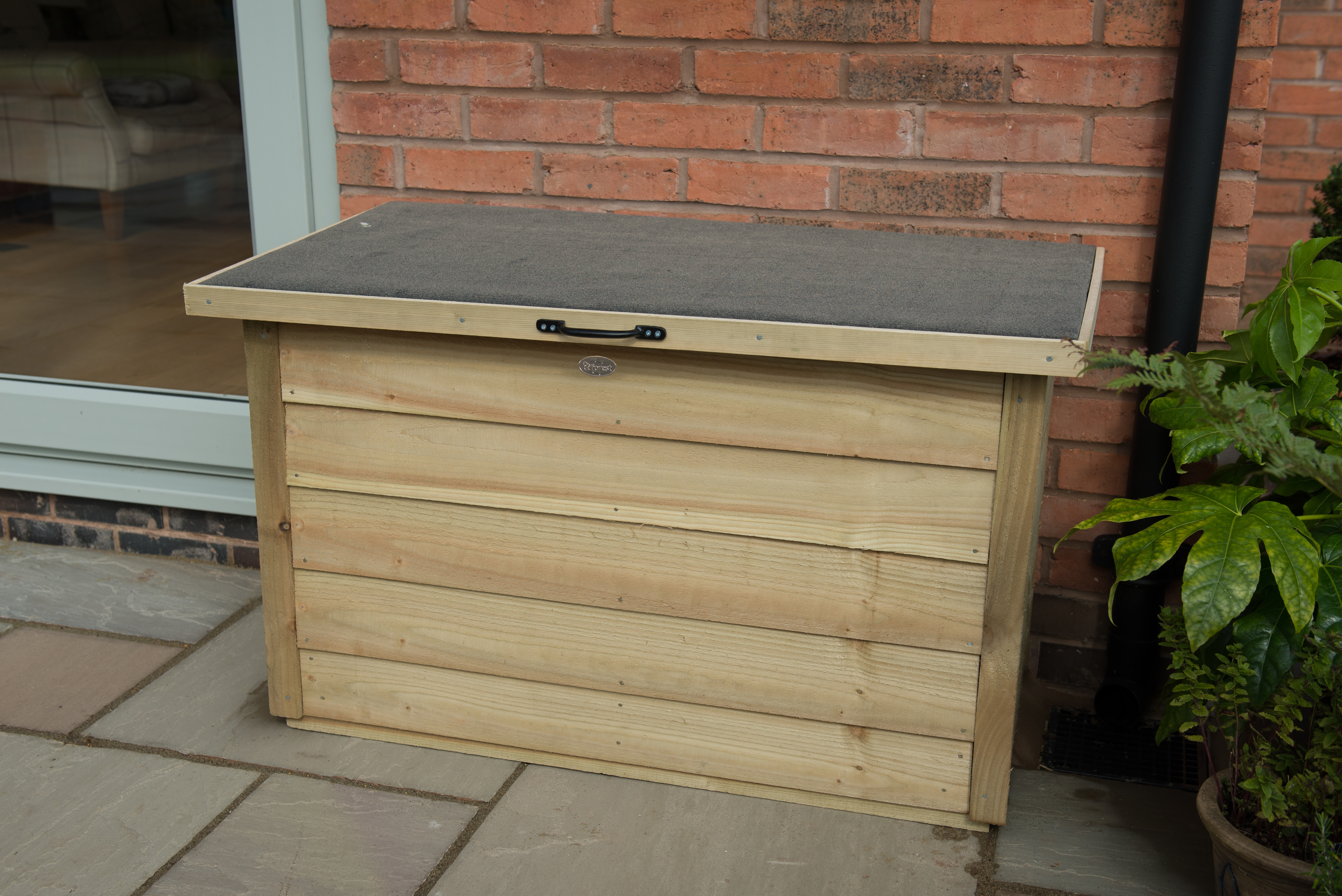 A timber garden storage box positioned outside surrounded by bright lights and fencing.