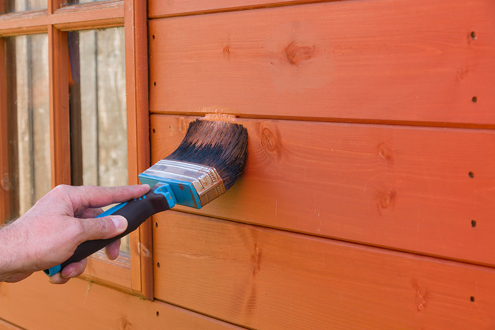 A paintbrush being used to put treatment on the exterior wall of a shed A paintbrush being used to put treatment on the exterior wall of a shed