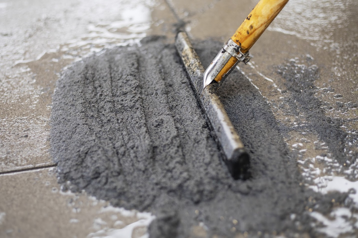 A person a brush to apply fresh grout in between the cracks of paving slabs for a patio to grout them.