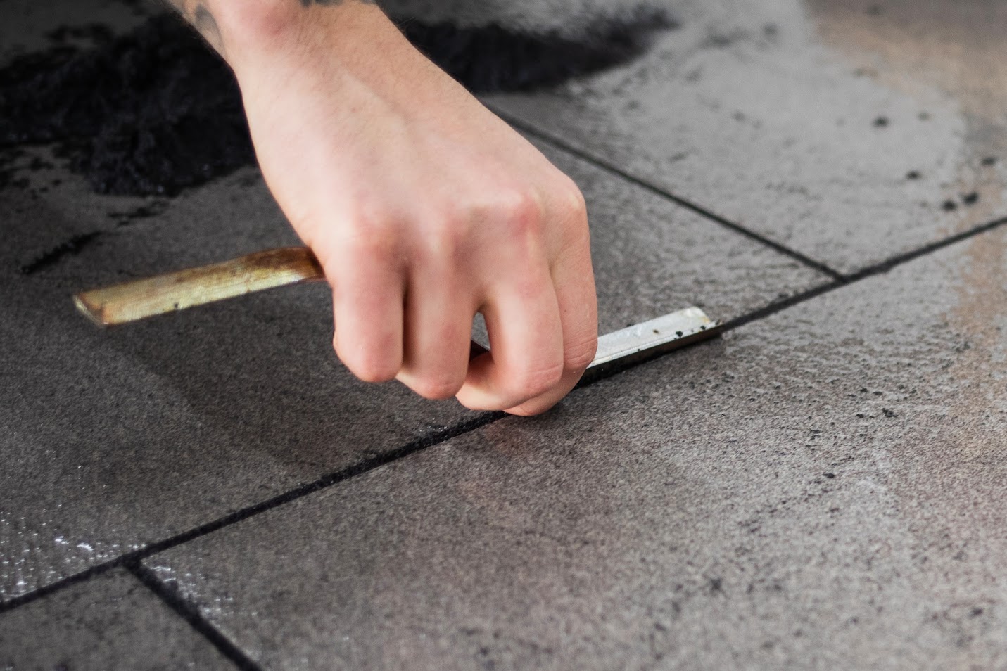 A man using a tool to smooth out grout in between cracks on paving. 