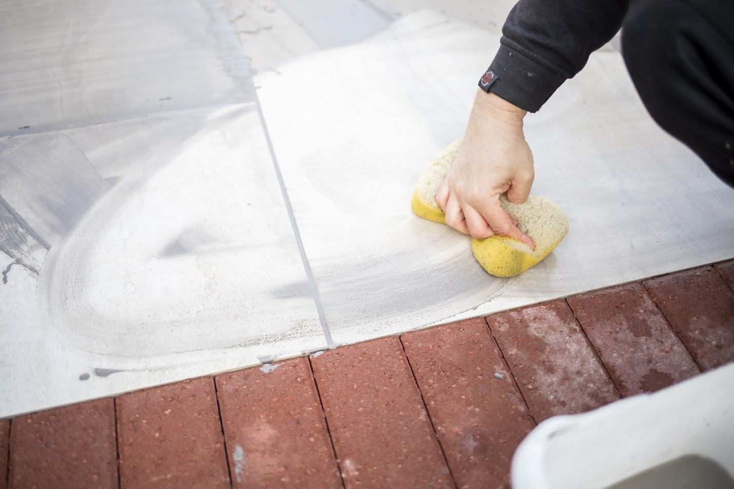 An image of a person with a sponge being used to effectively clean and maintain pacing and block paving by getting rid of oil stains, algae and dirt.