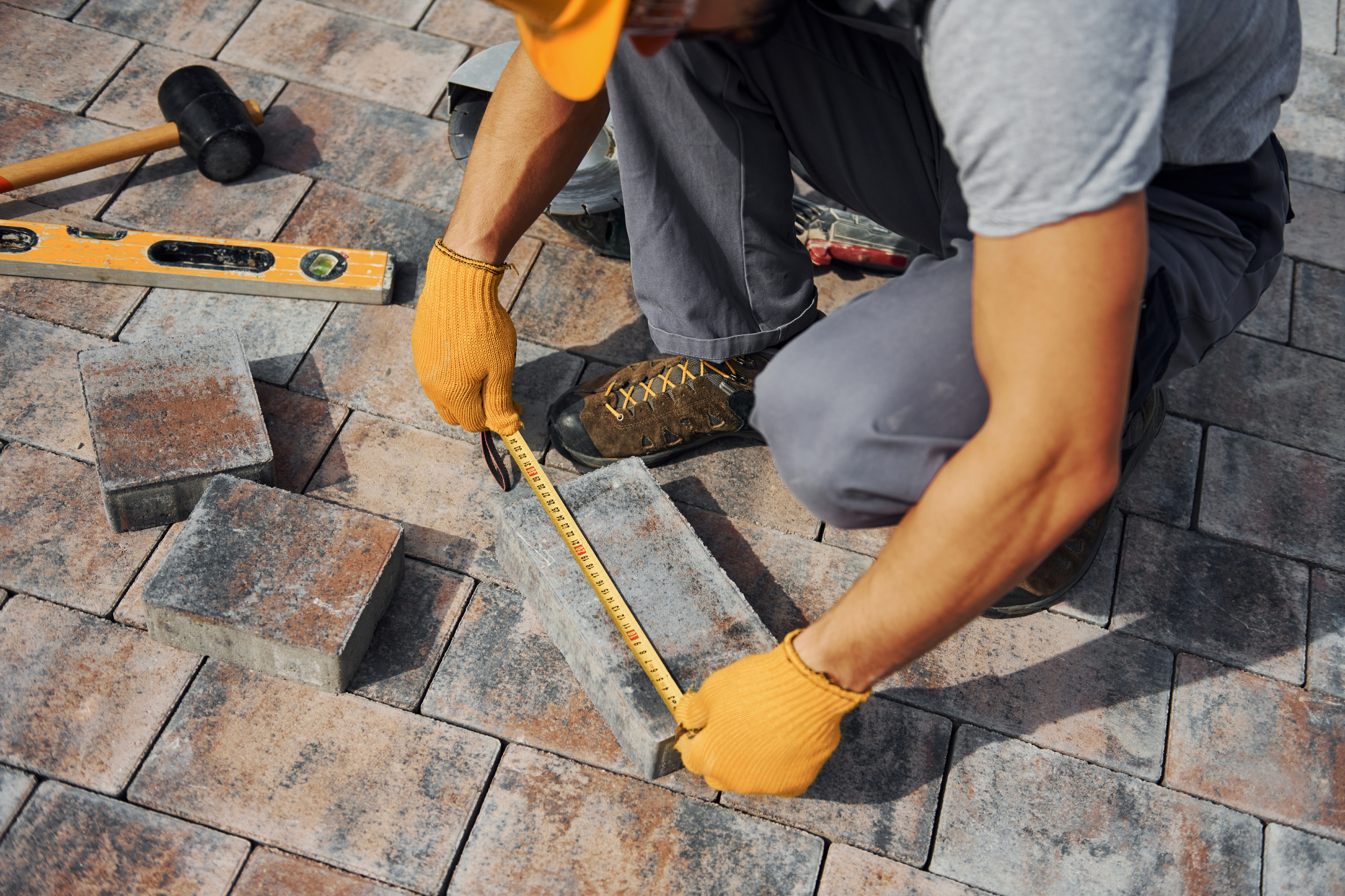 Person measuring paving slabs with a tape measure, preparing for installation in a landscaped outdoor area.