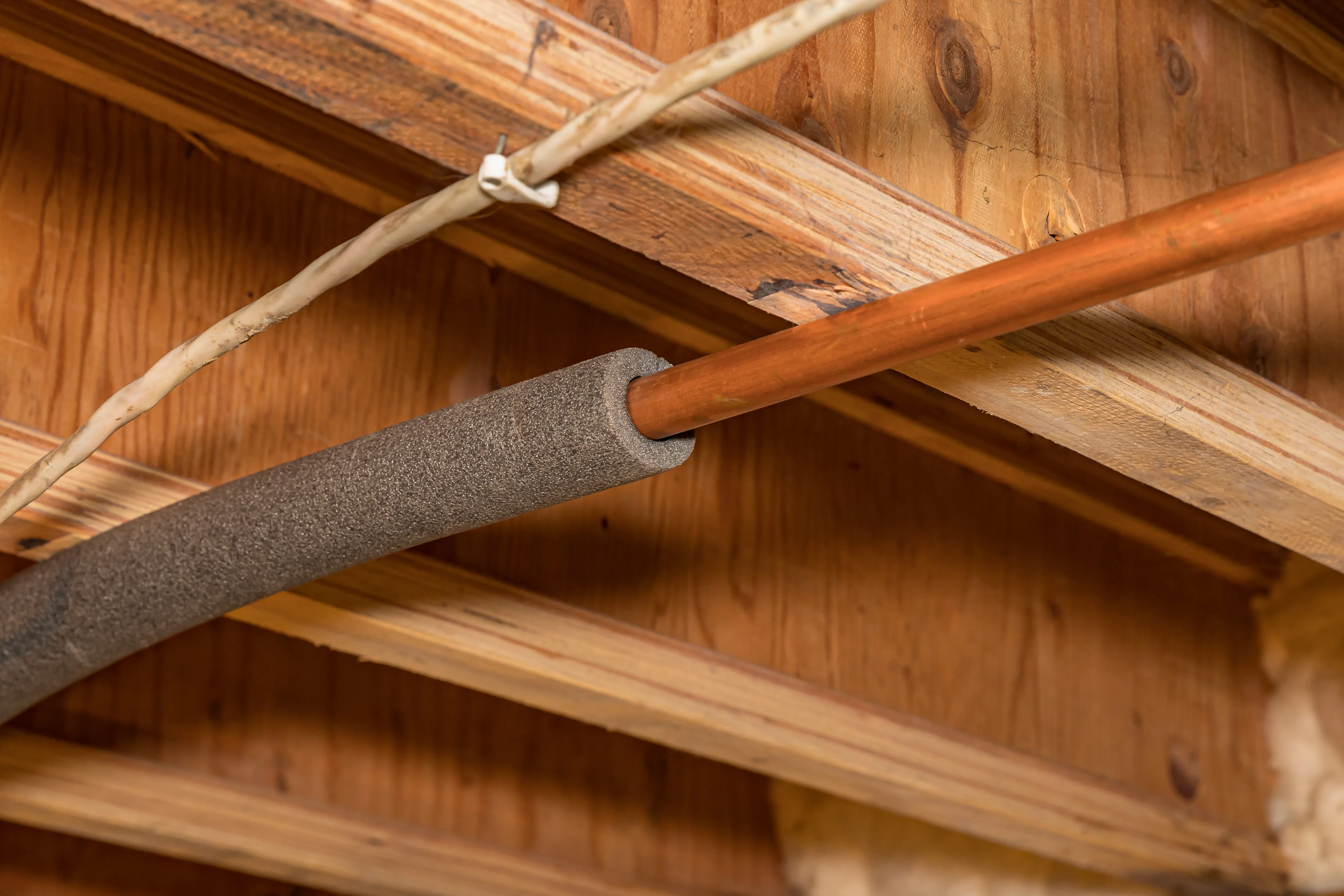An image of insulation wrapping around a pipe in the roof of a home.