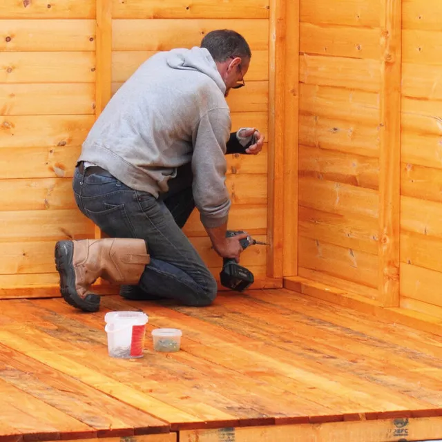 Man on the outside of a shed, using stain to weatherproof it. Man on the outside of a shed, using stain to weatherproof it.