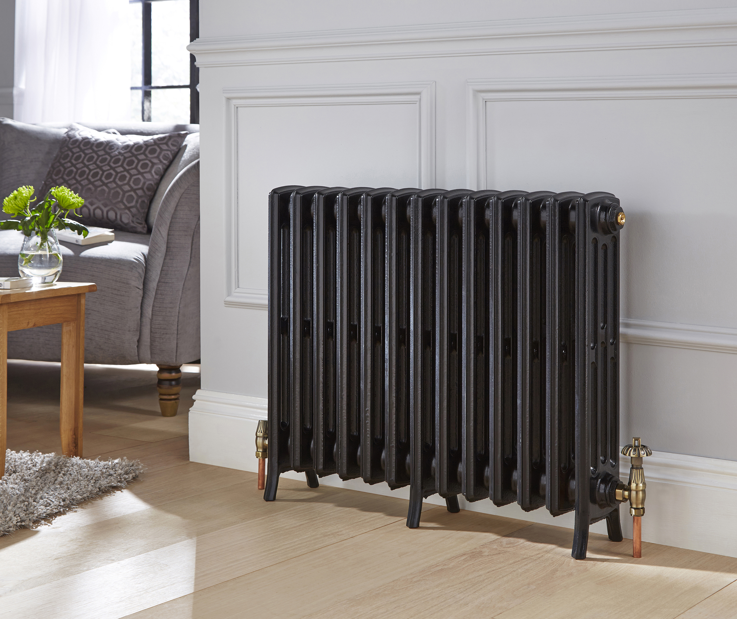 A black cast iron radiator hung against a wall panelled wall with a sofa in the background. 
