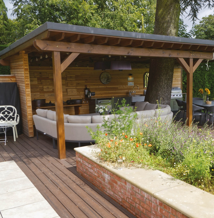 A luxurious outdoor kitchen with circular seating underneath a pergola.