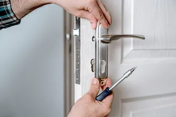 A door handle being installed to a white, modern door with a screwdriver.