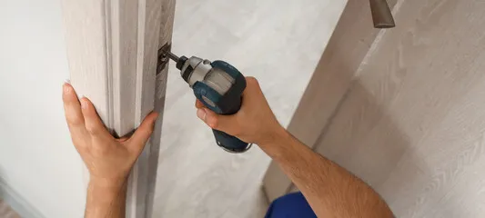 A drill being used to install a door into a home, with the hinges being drilled into.