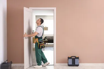 A man installing a door in a modern home. With beige walls and a white door.