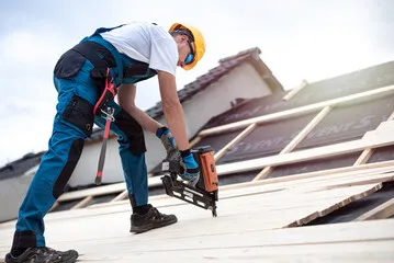 A man drilling into a roof with roof battens appearing behind.