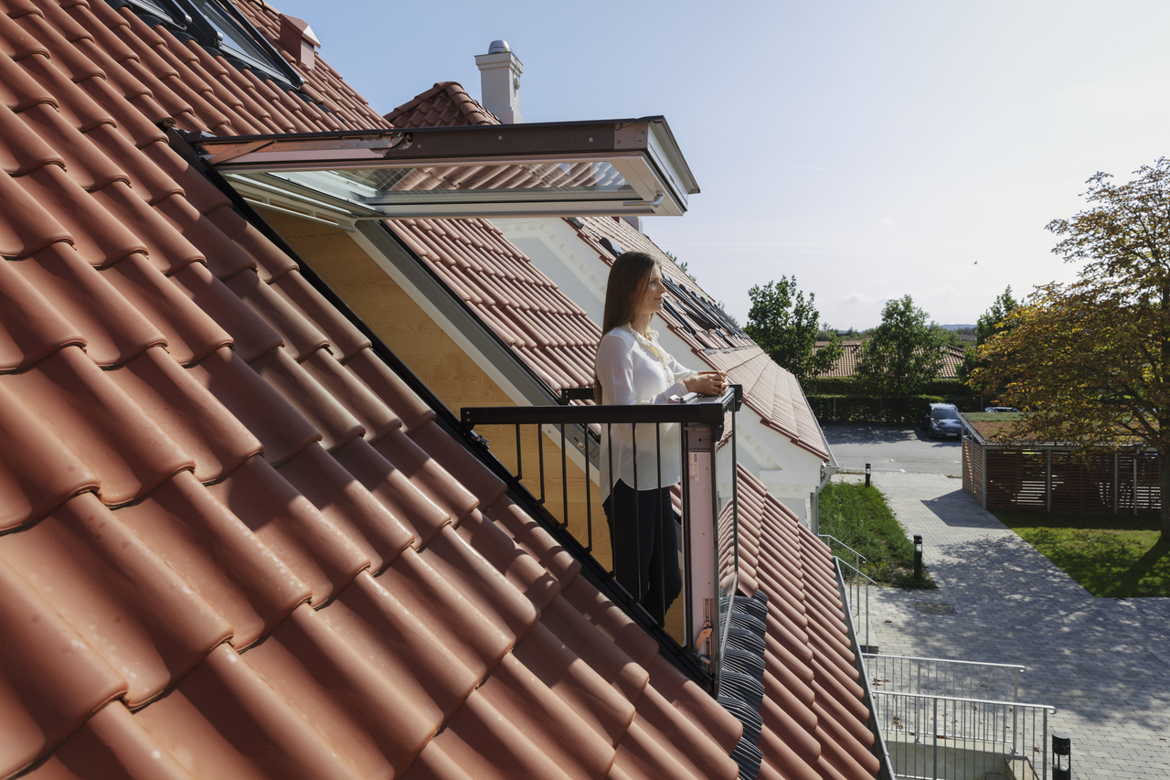 A woman standing on a VELUX balcony window, looking out from her roof.