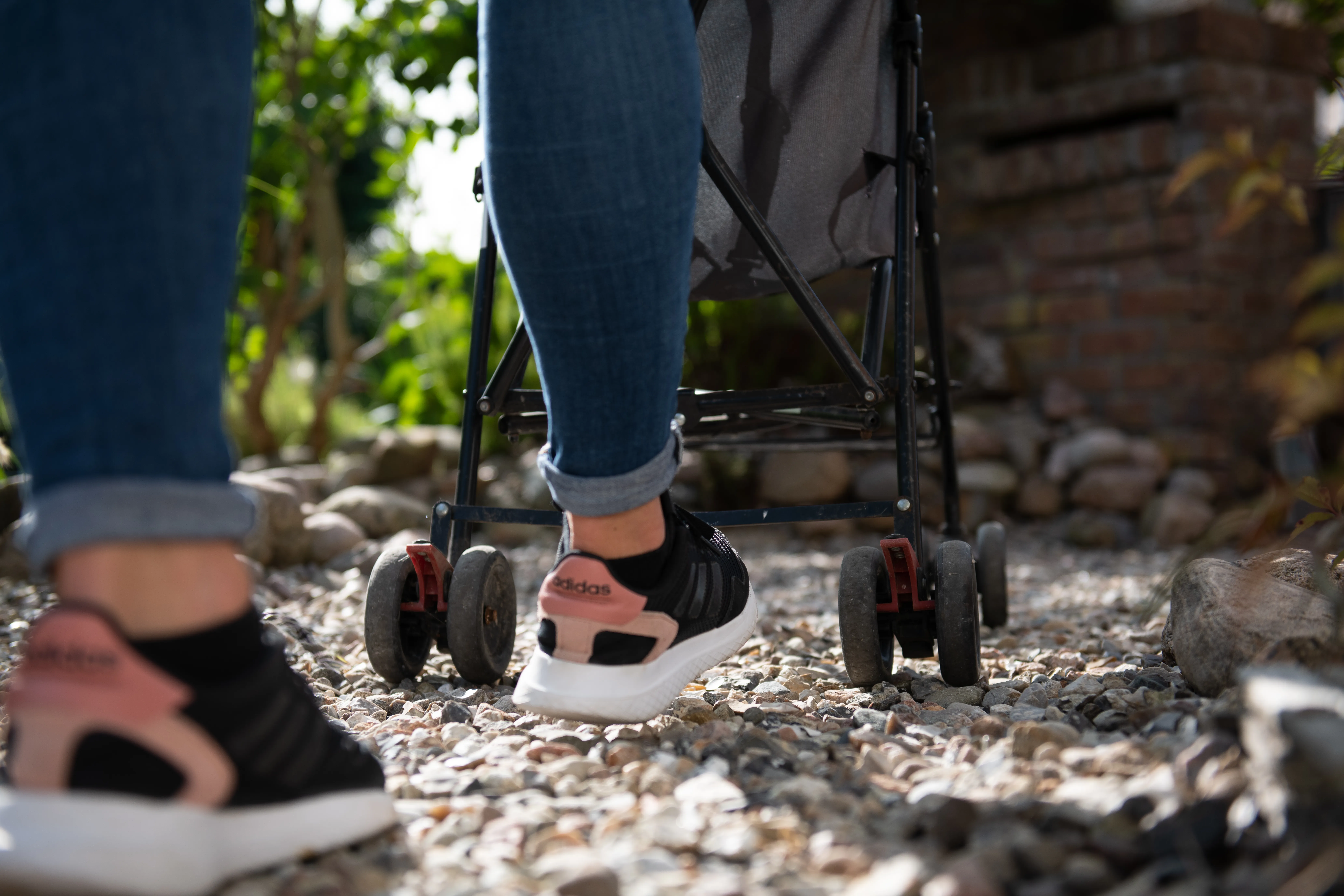 Image of a woman and a pram walking across some gravel.
