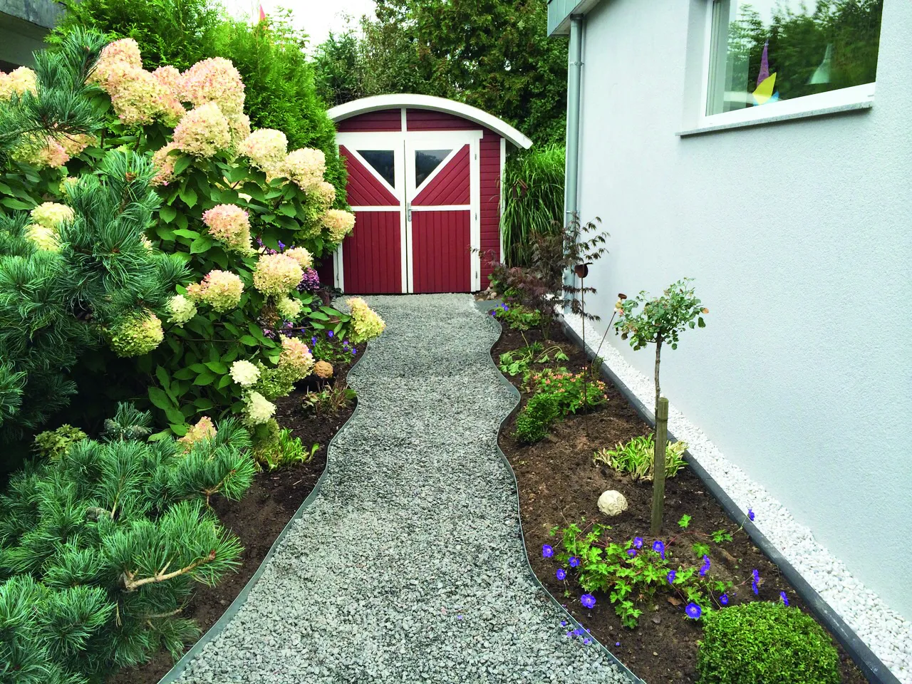 Image of a gravel pathway leading to a red cottage shed at the end of the garden.