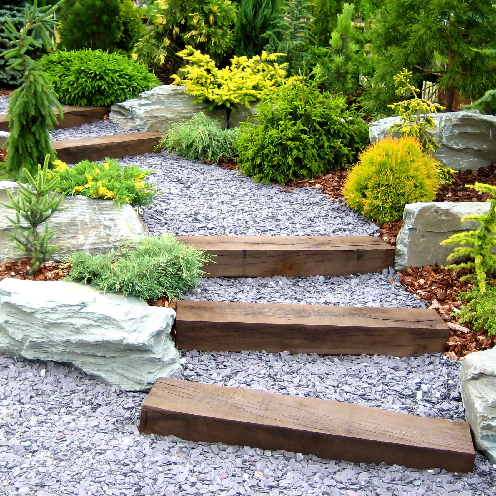 Image of a gravel steps leading up to the top of a garden with shrubbery surrounding it.