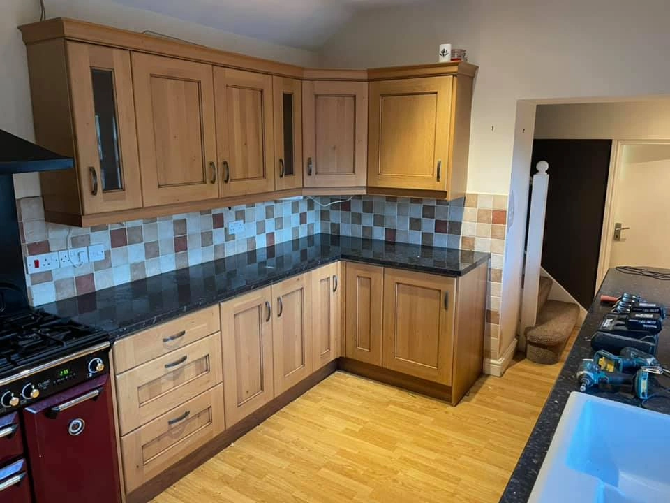 Traditional looking kitchen with wooden cabinets and cupboards, red detailing, white walls and tiling, and black worktops.
