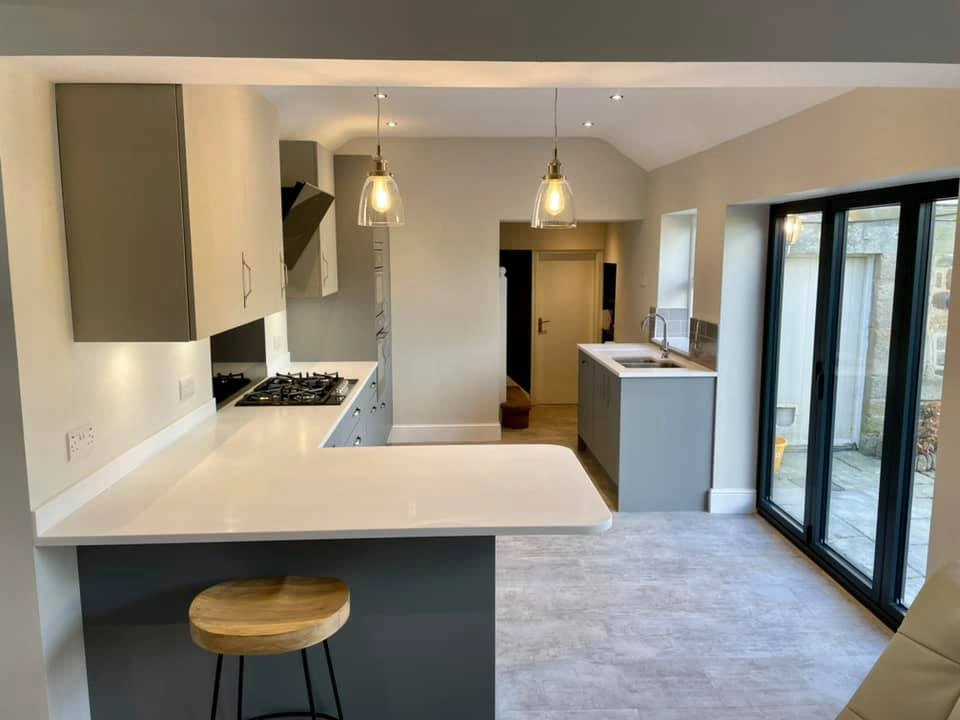 A modern bathroom with modern lighting, white granite worktops, black patio doors and small breakfast bar.