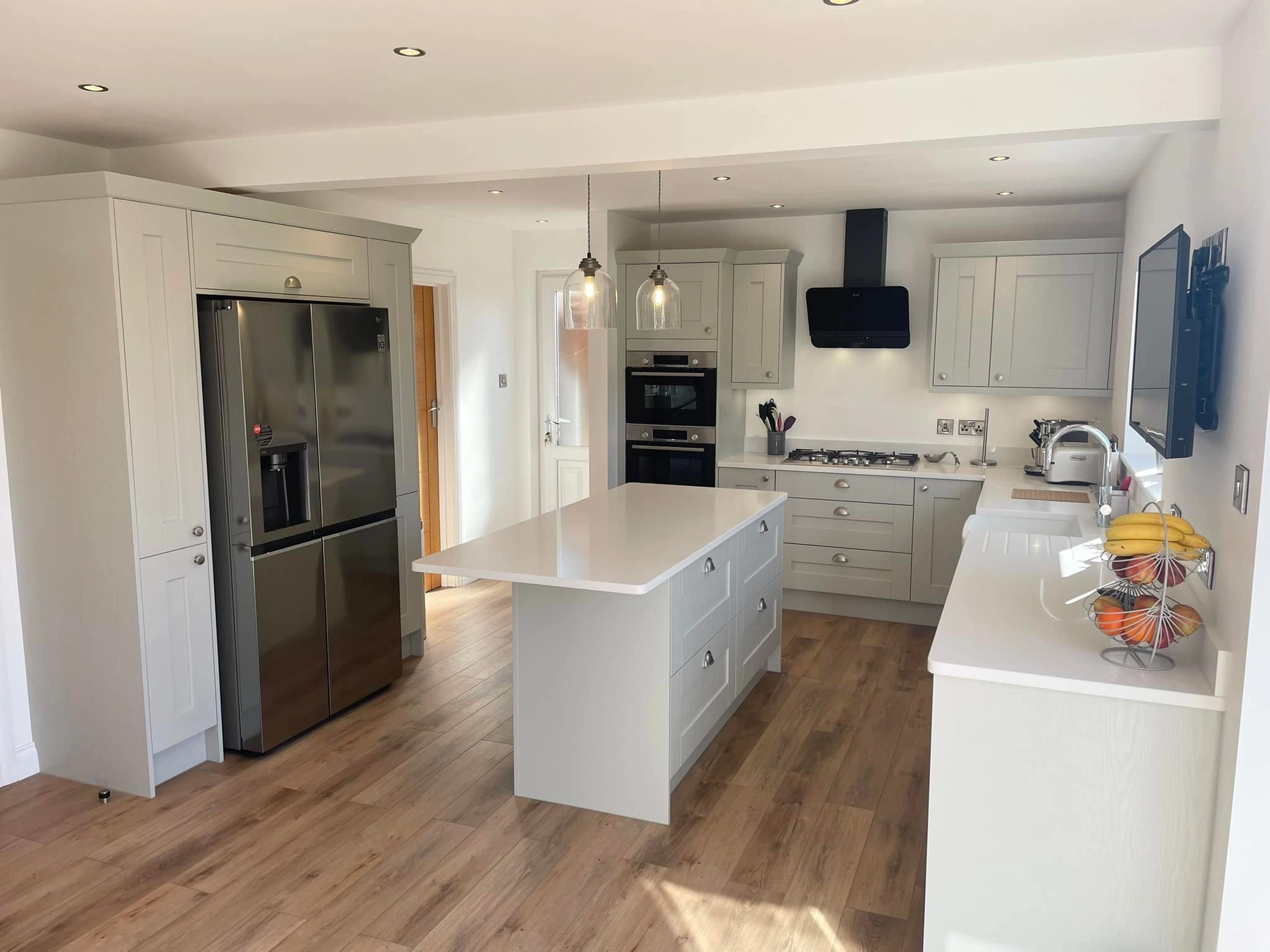 An enlarged kitchen space, with wide fridge, kitchen island, and white details and worktops. 