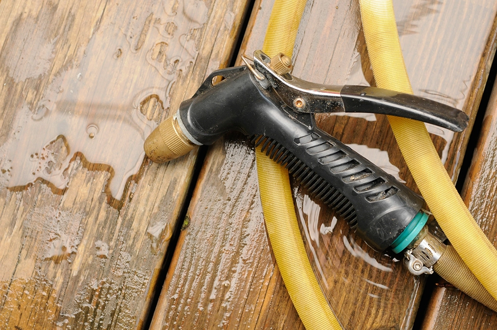 A hosepipe being used to spray down a deck so that it maintains clean and well-maintained. 