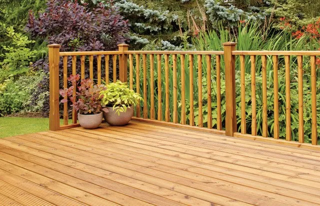 Image of some decking in a garden, with railings and a green plantpot in the corner.