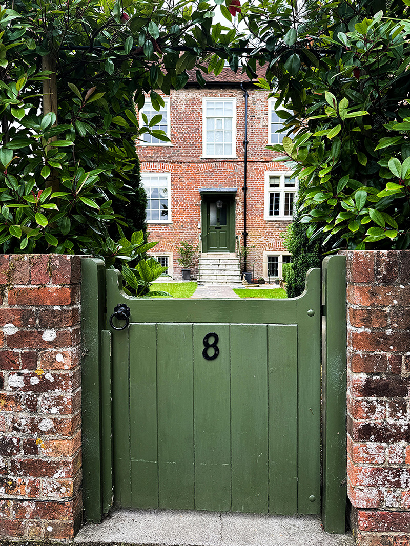 an image of a white garden gate outside a cottage home, with a lime door