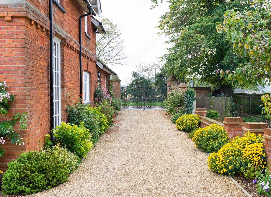 a caramel coloured gravel driveway at the side of a cottage style house
