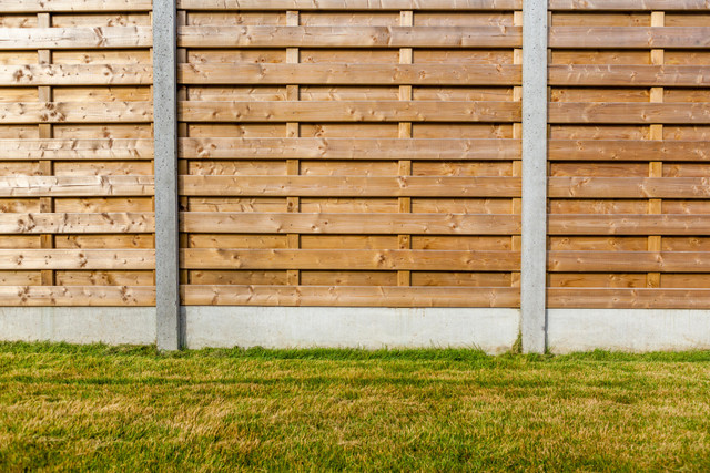 A person using a paint brush to paint a garden fence with a blue sky background. 
