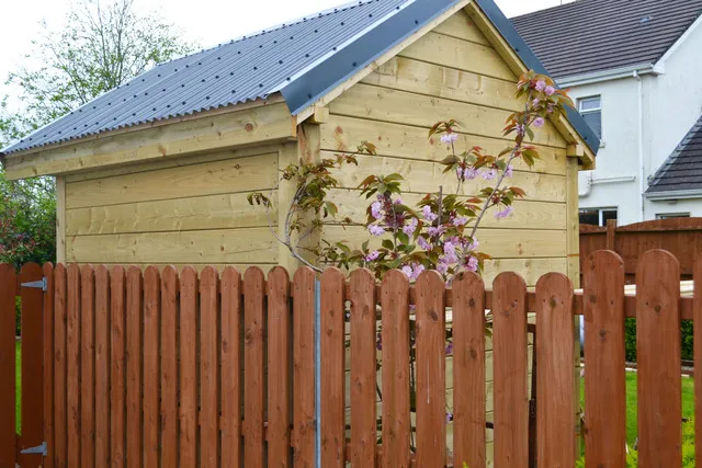 Dark-brown fence posts alligning a shed in someones garden.