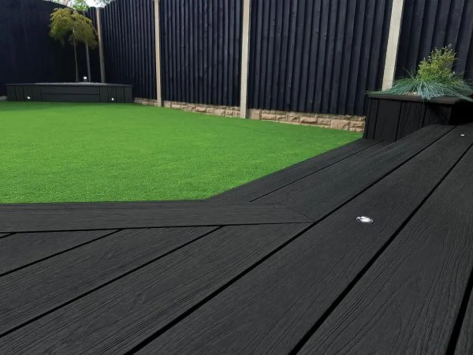 Black-coloured composite decking in a garden alongisde a fence.