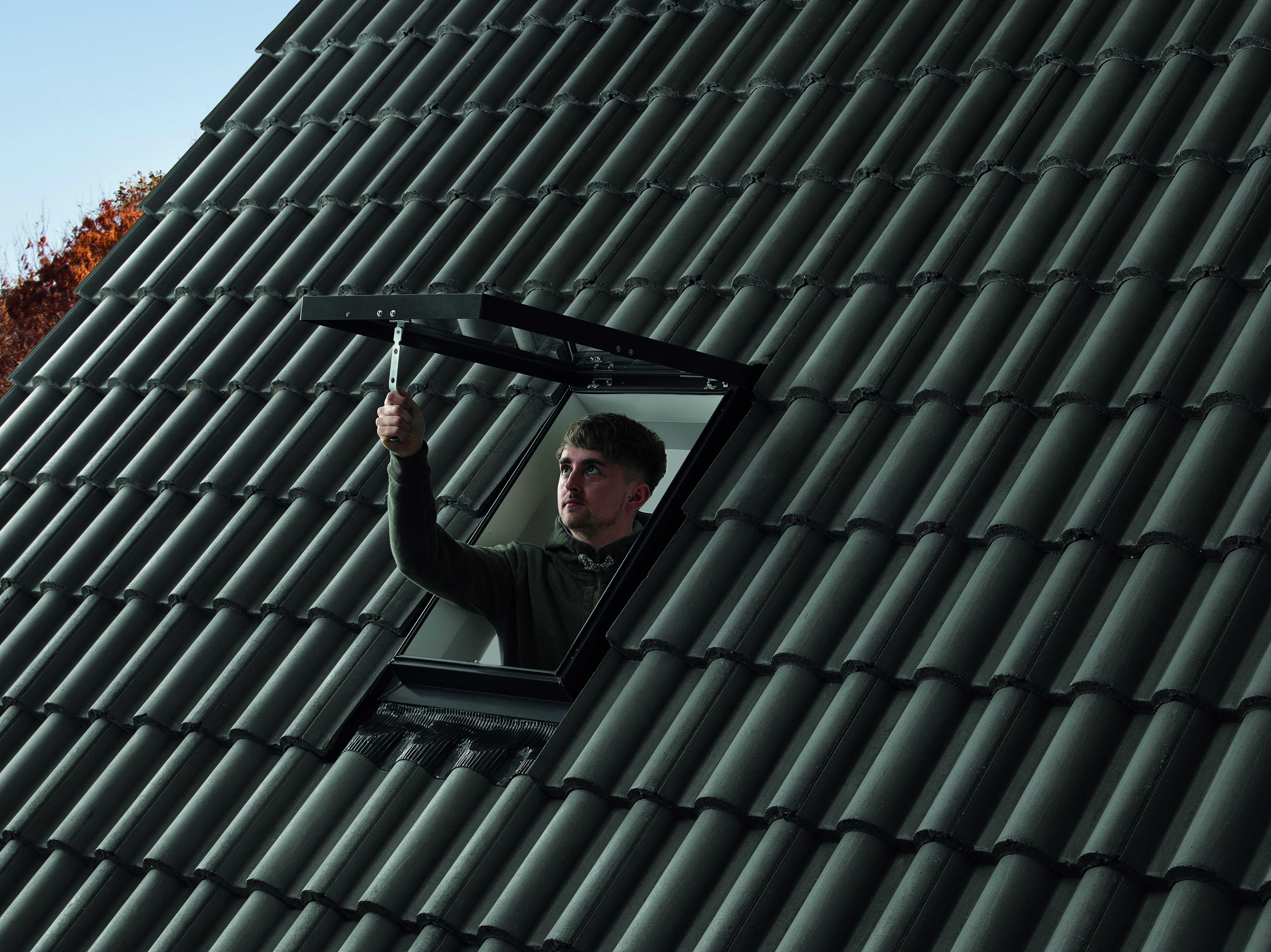 A woman using  a roof window by opening it from her attic and looking out from it.