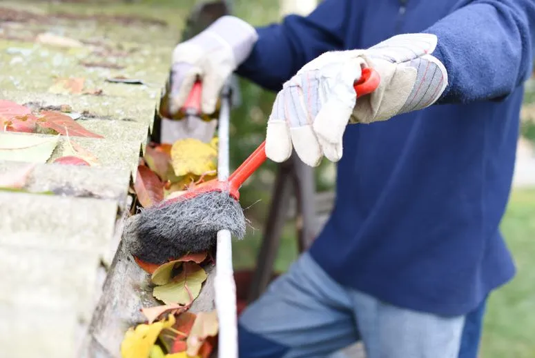 A man using tools to remove waste, leaves and debris from a gutter in a home. A man using tools to remove waste, leaves and debris from a gutter in a home.