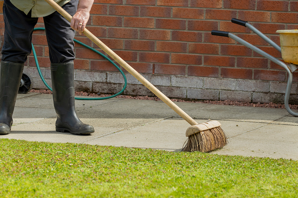 A person using a garden brush to brush down their patio to prepare for the winter months ahead.