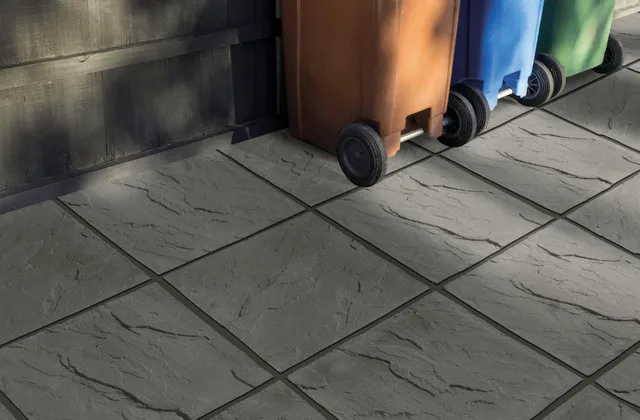 A close-up image of some paving used outside, with some wheelie bins in the top right side.