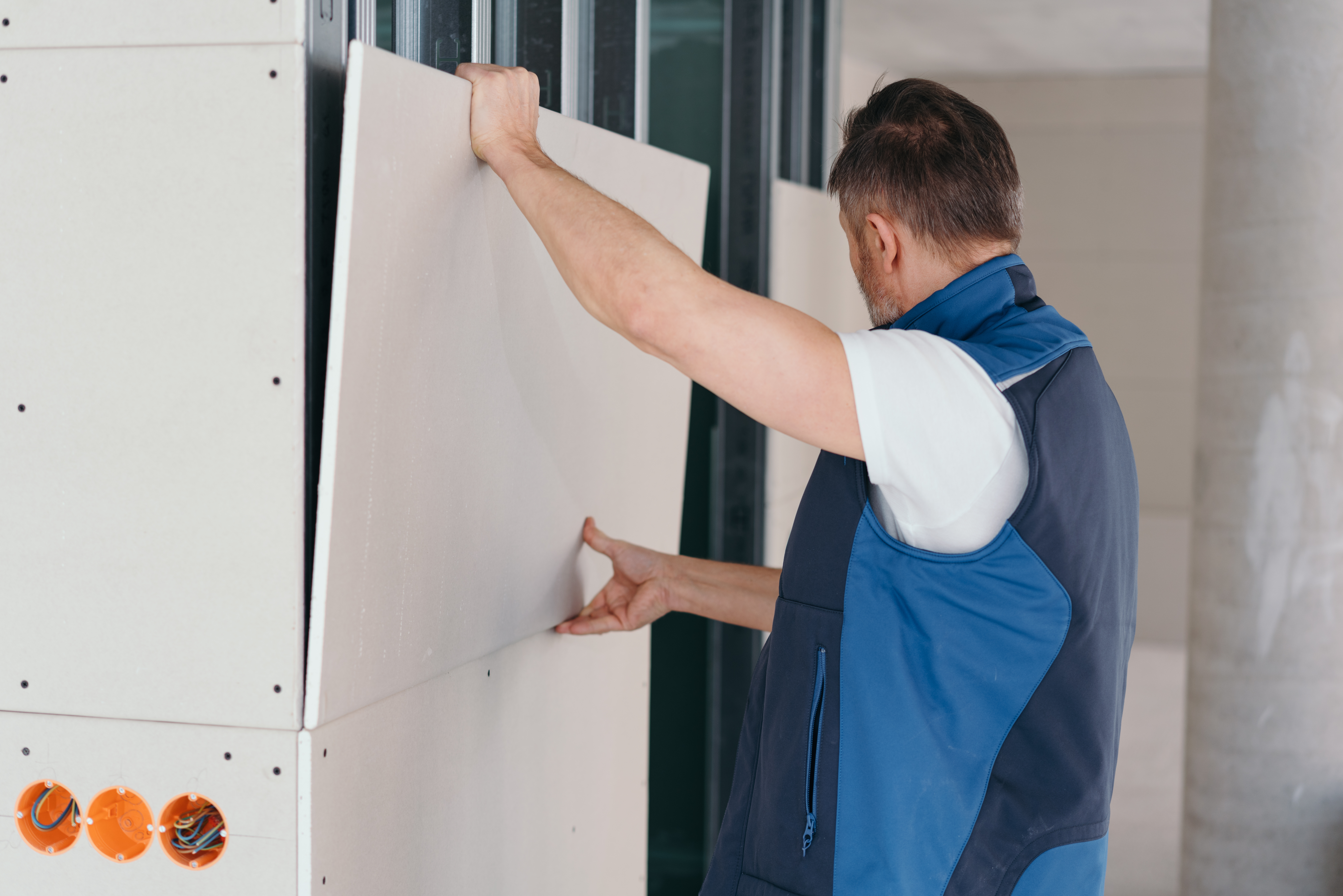 A man using gloves hands to attach plasterboard to wall.