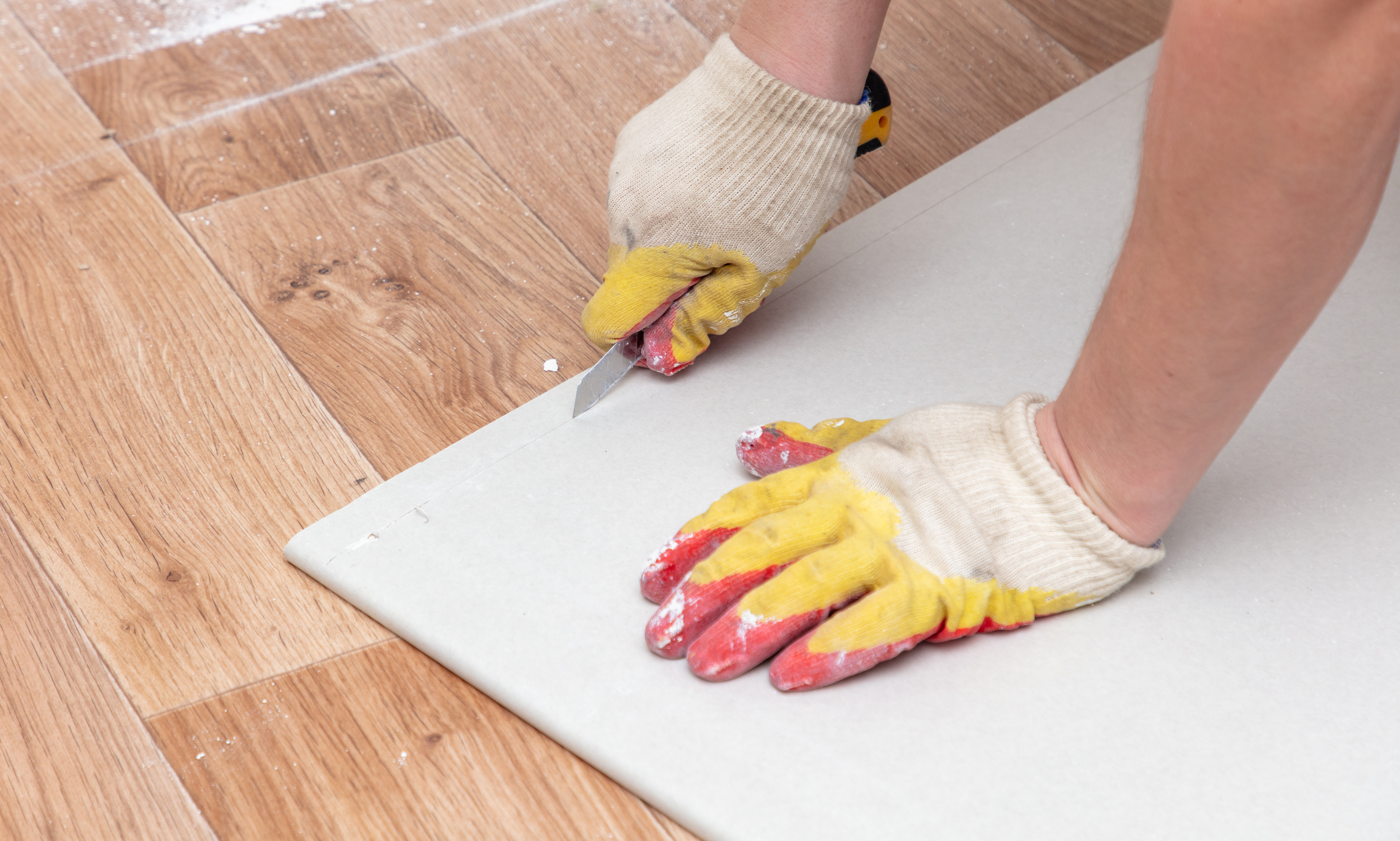 Hands using a stanley knife to cut into plasterboard.