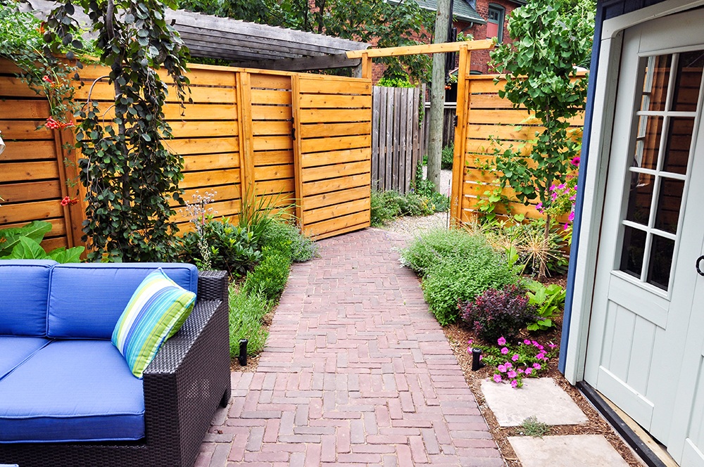 an image of a charcoal grey paneled fence with grey timber posts amongst a green grass garden. 